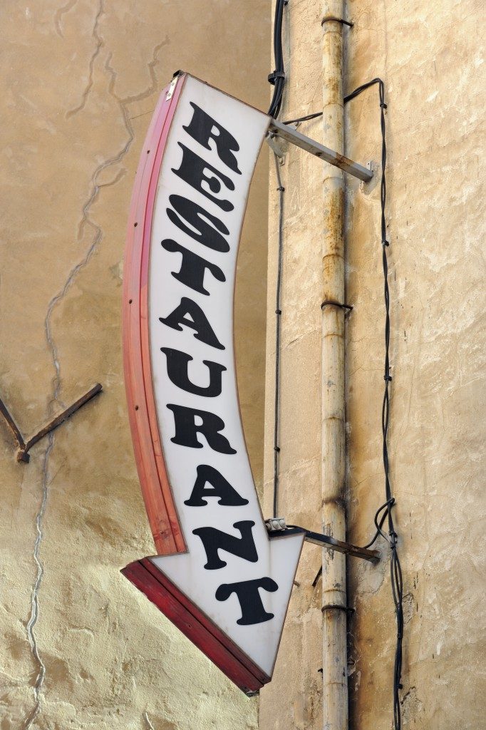 Restaurant arrow sign, black writing on white background, with ochre painted wall behind