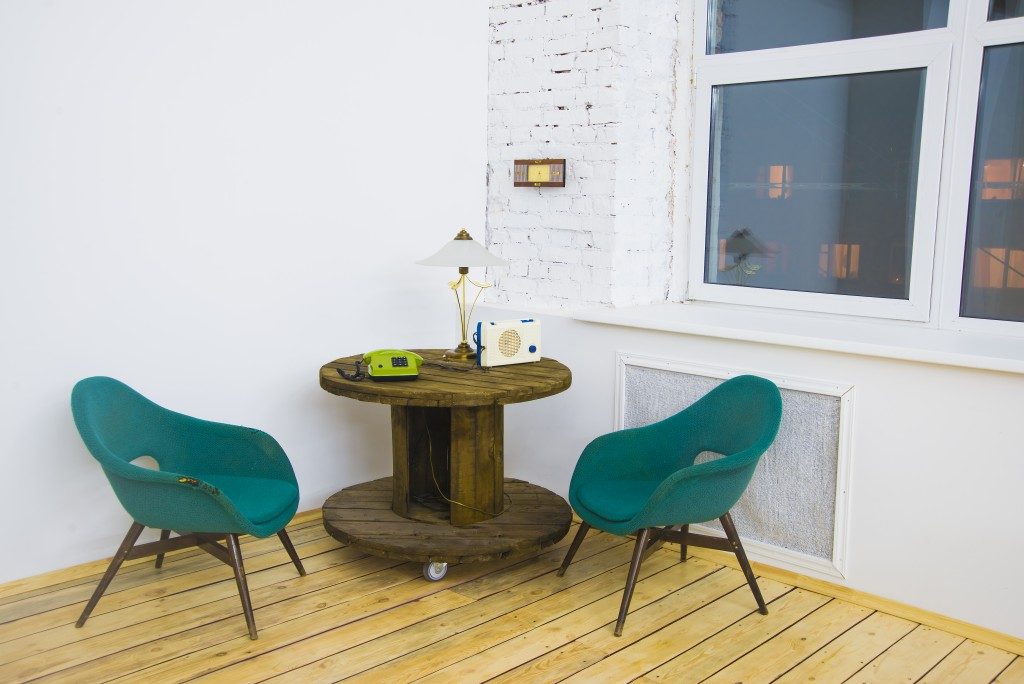  two soft green chair with wooden circle table and phone, lamp, radio on table
