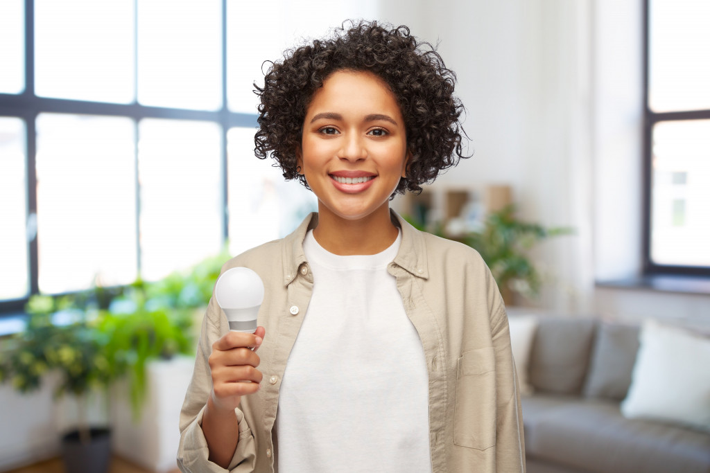 happy smiling woman holding lighting bulb over home background